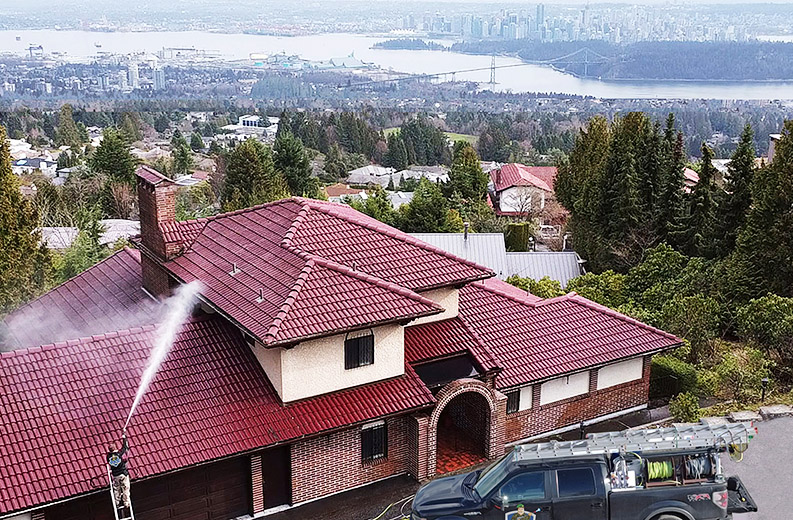 a drone photo of a clean squad employee spraying soft wash solution onto a concrete roof in west vancouver overlooking downtown vancouver