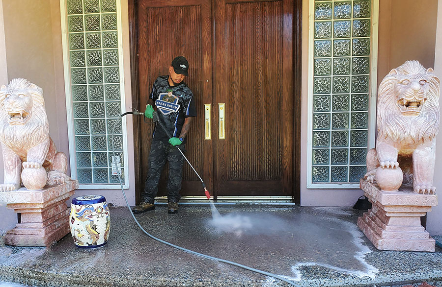 a clean squad employee pressure washing the concrete entrance to a luxury vancouver home. there are two granite dragon statues in the doorway.