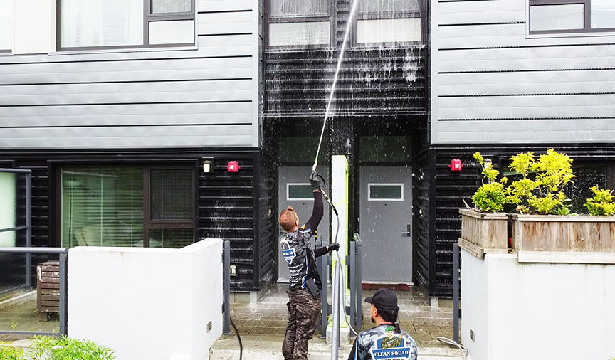 two clean squad employees soft washing a large townhouse building