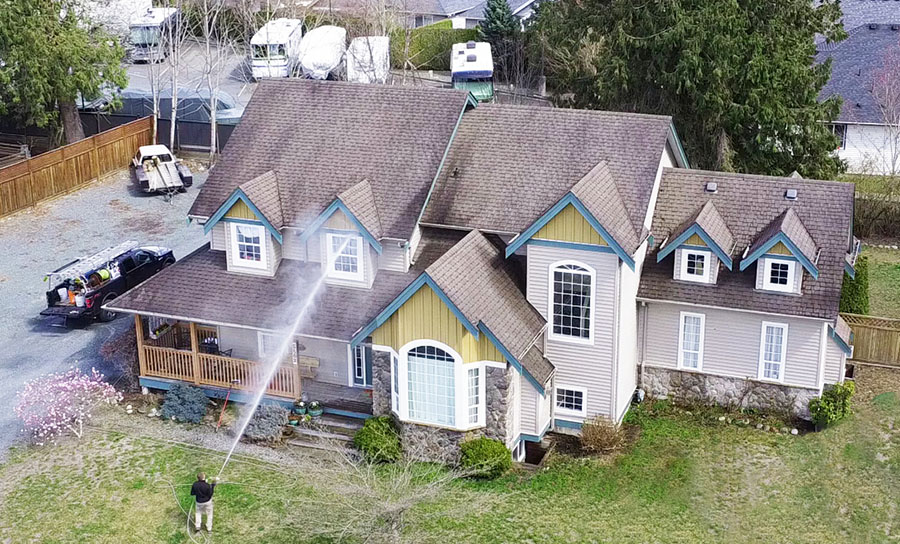 a drone photo of a clean squad employee soft washing a large vinyl house