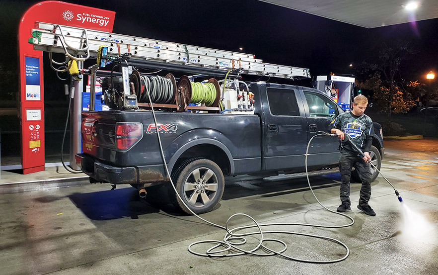 clean squad team member power washing gas station at night